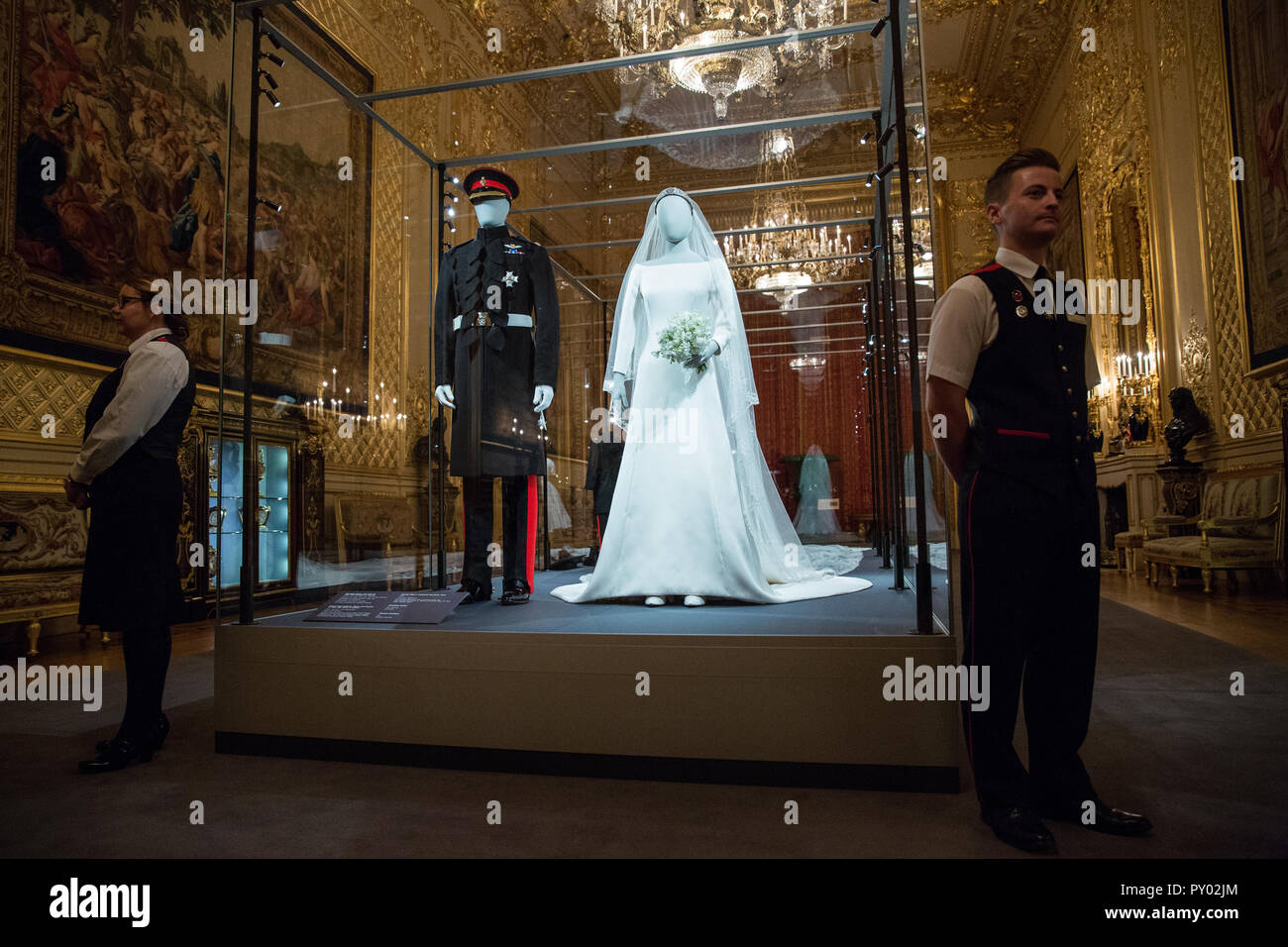 Windsor, UK. 25th October, 2018. IMAGE EMBARGOED FOR PUBLICATION UNTIL 00:01 BST, FRIDAY, 26 OCTOBER. Windsor Castle staff members pose next to the Duchess of Sussex’s wedding dress, created by the British designer Clare Waight Keller, Artistic Director at the historic French fashion house Givenchy, and the Duke of Sussex's frockcoat uniform of the Household Cavalry, which will go on display from 26th October 2018 to 6th January 2019 as part of a special exhibition entitled 'A Royal Wedding: The Duke and Duchess of Sussex'. Credit: Mark Kerrison/Alamy Live News Stock Photo
