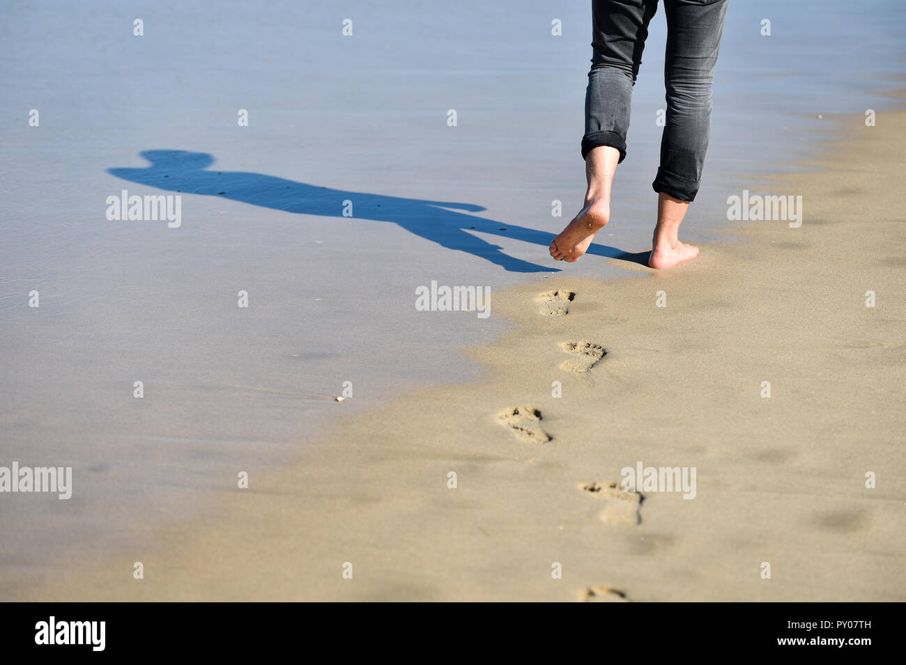 Man walking barefoot making footprints in the sand on a beach Stock ...