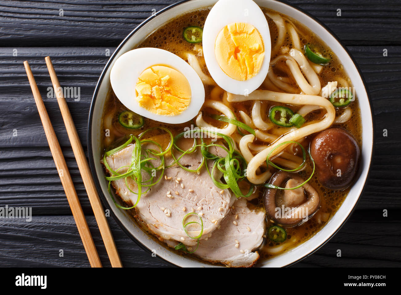 Spicy udon noodle soup, pork, boiled eggs, shiitake and onions closeup