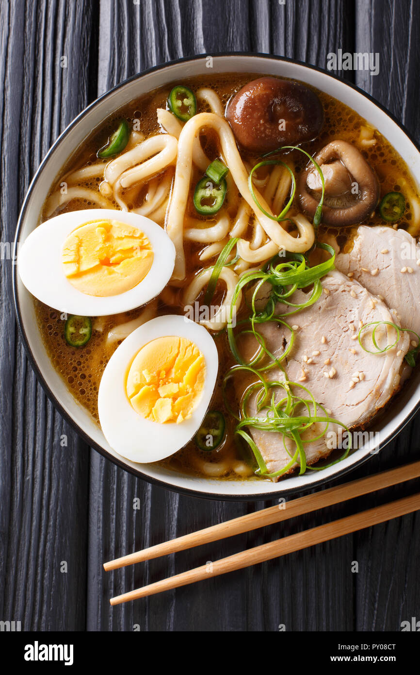 Traditional Japanese udon noodle soup with pork, boiled eggs, mushrooms and green onions closeup in a bowl on the table. Vertical top view from above Stock Photo