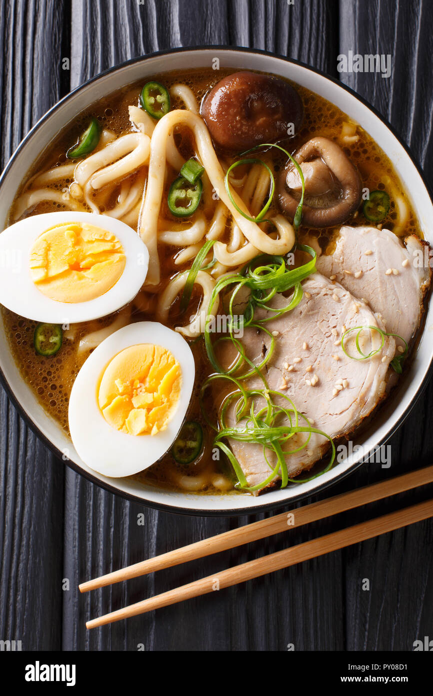 Spicy udon noodle soup, pork, boiled eggs, shiitake and onions closeup