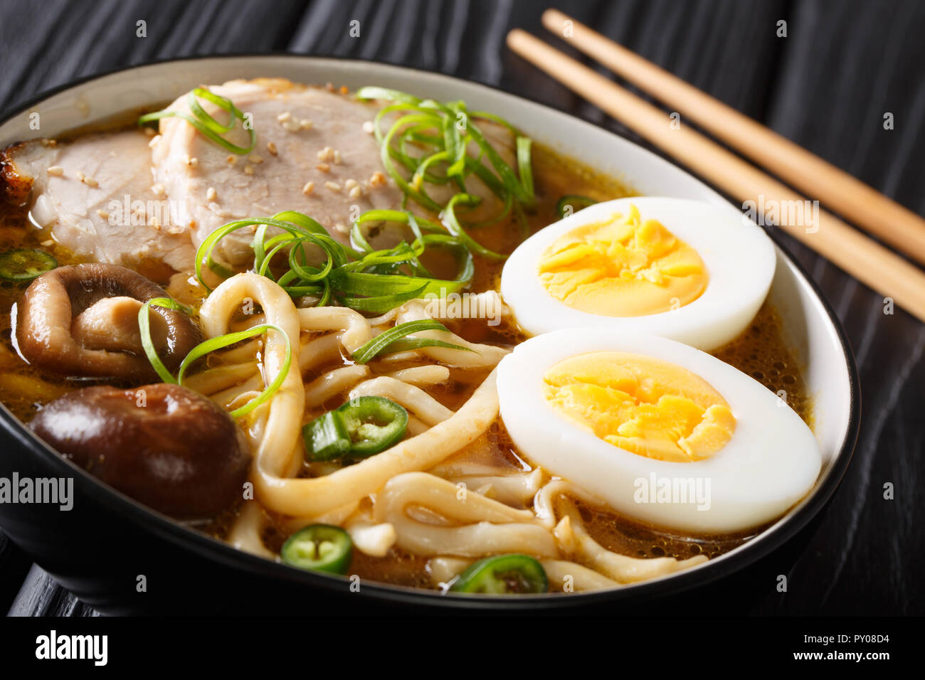Spicy udon noodle soup, pork, boiled eggs, shiitake and onions close-up in a bowl on the table. horizontal Stock Photo