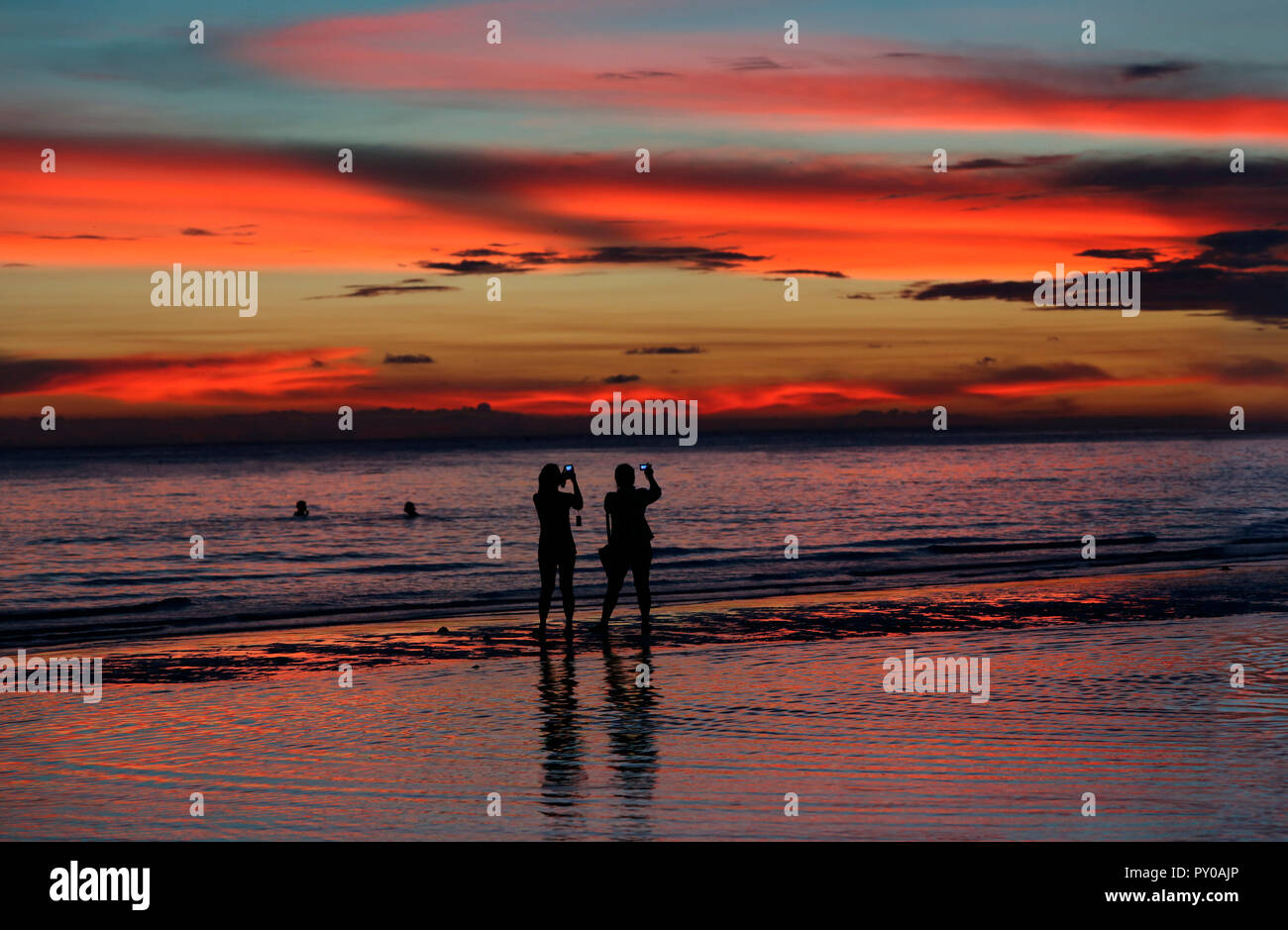 Silhouettes of two female tourists photographing sunset on beach, Boracay, Aklan, Philippines Stock Photo