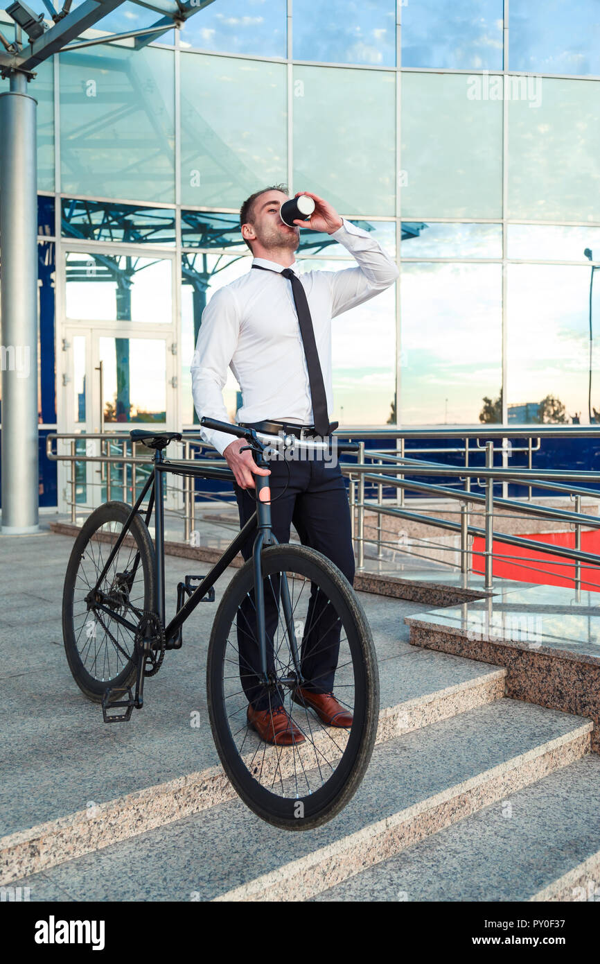 Man in suit holding a cup of coffee walking by the street with his bicycle. Stock Photo