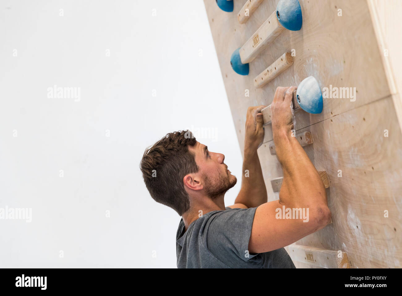 Strong man training on wooden rail in rock climbing gym against white wall, Oahu, Hawaii, USA Stock Photo
