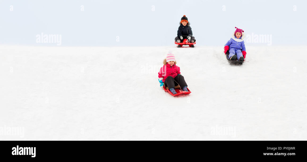 kids sliding on sleds down snow hill in winter Stock Photo