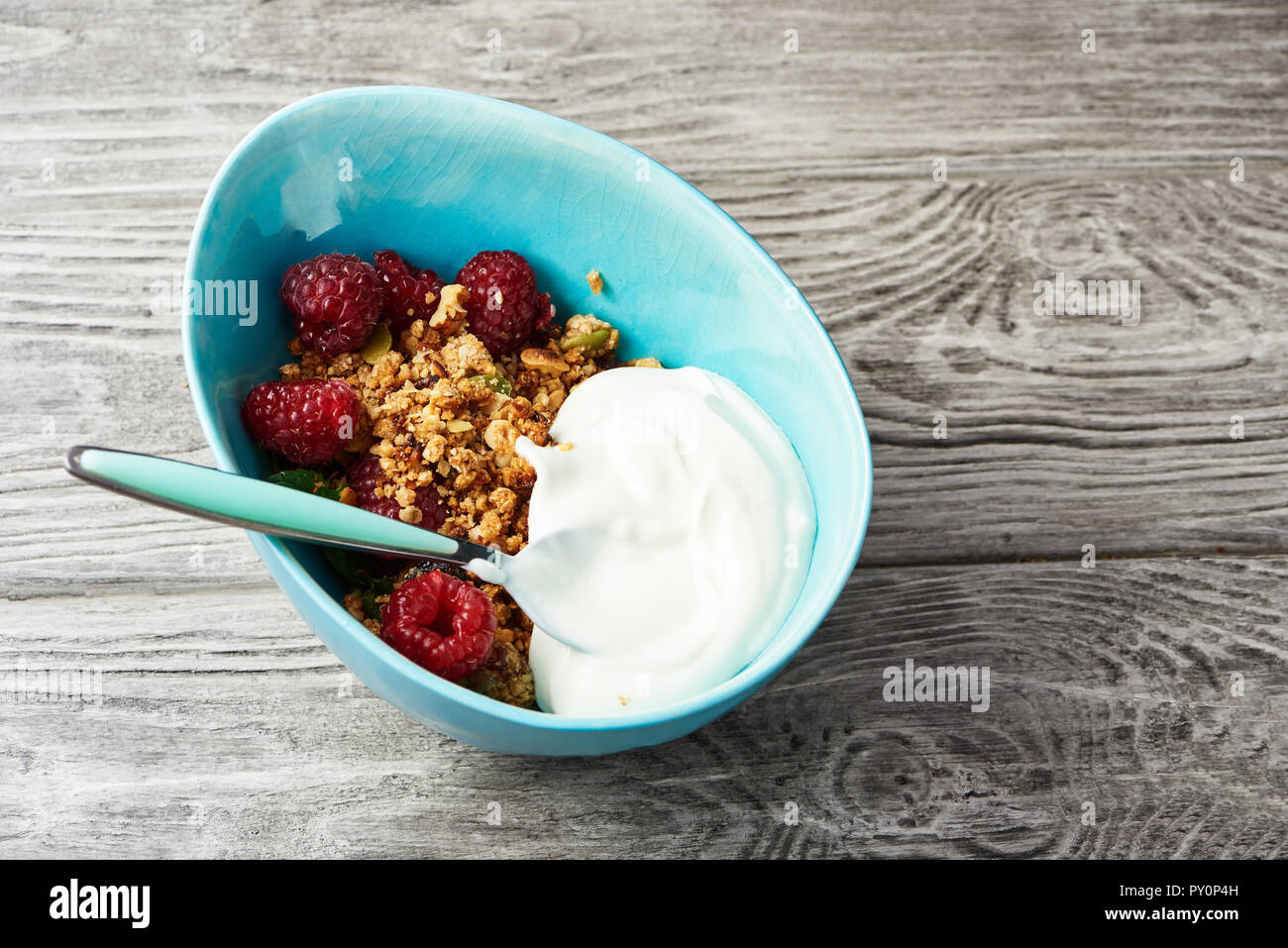 Homemade granola with yogurt in a bowl with raspberries on a wooden table. Stock Photo
