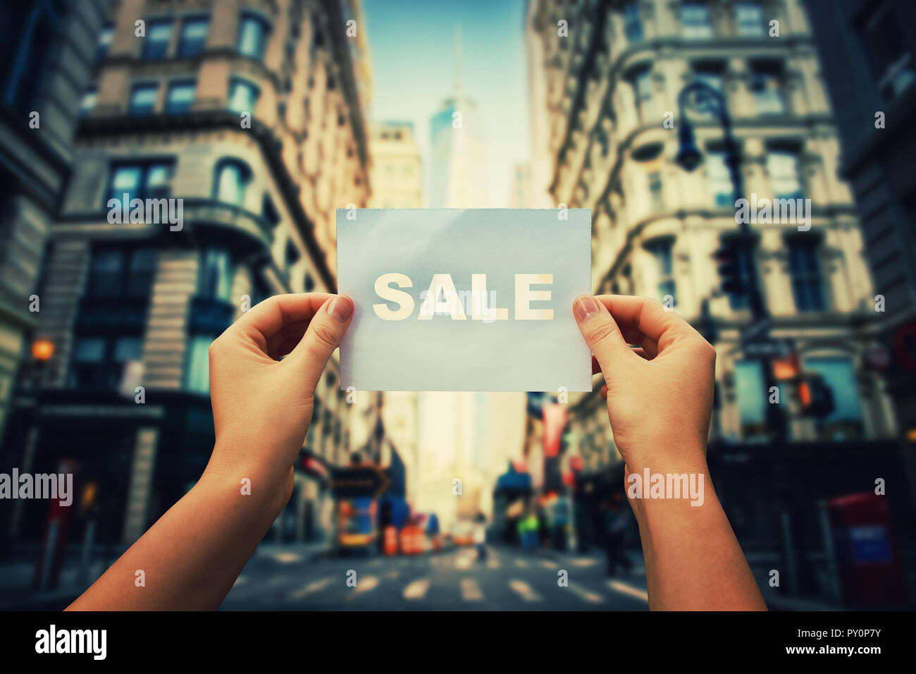 Woman hands holding a paper sheet with sale word in the middle of the big city street. Seasonal shopping time, black friday announcement, special offe Stock Photo