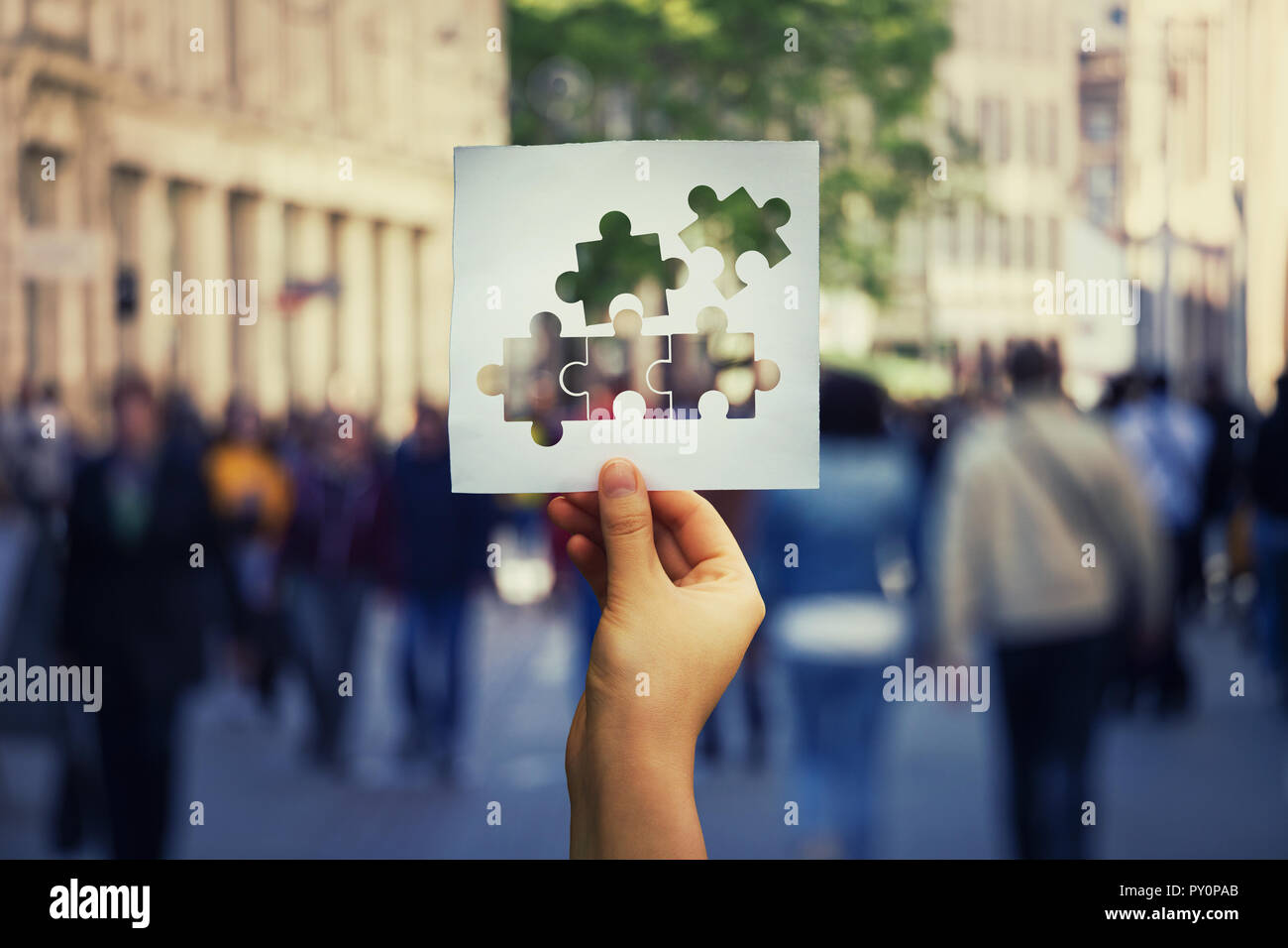 Hand holding a paper sheet with connecting jigsaw puzzle over a crowded street background. Business solutions, success and strategy. Teamwork connecti Stock Photo
