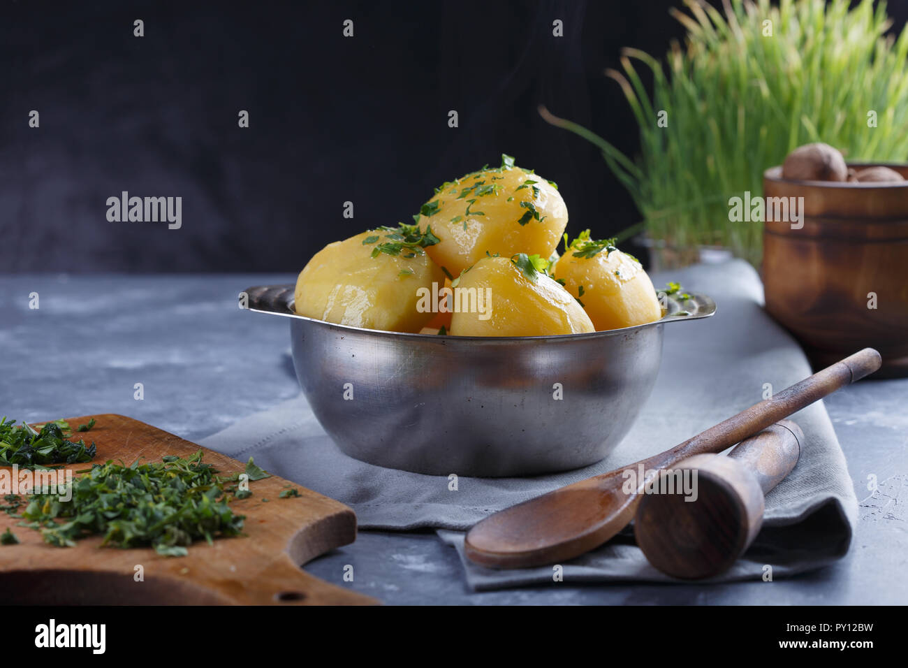 Hot boiled potatoes in a plate dusted with greens and smoke on a gray background. Stock Photo