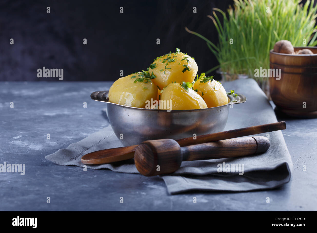 Hot boiled potatoes in a plate dusted with greens and smoke on a gray background. Stock Photo