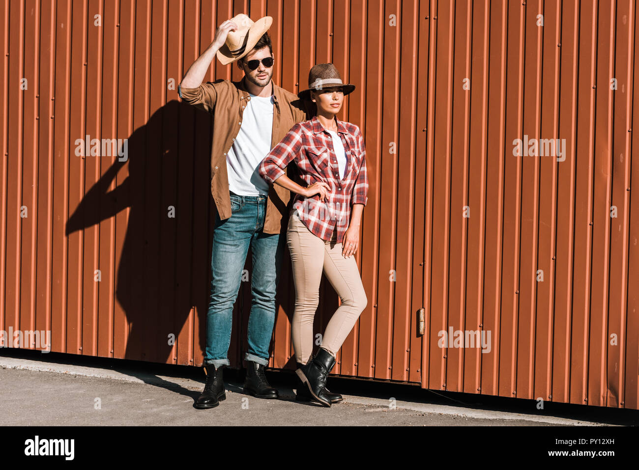 cowboy and cowgirl in casual clothes leaning on brown wall and looking away  at ranch Stock Photo - Alamy