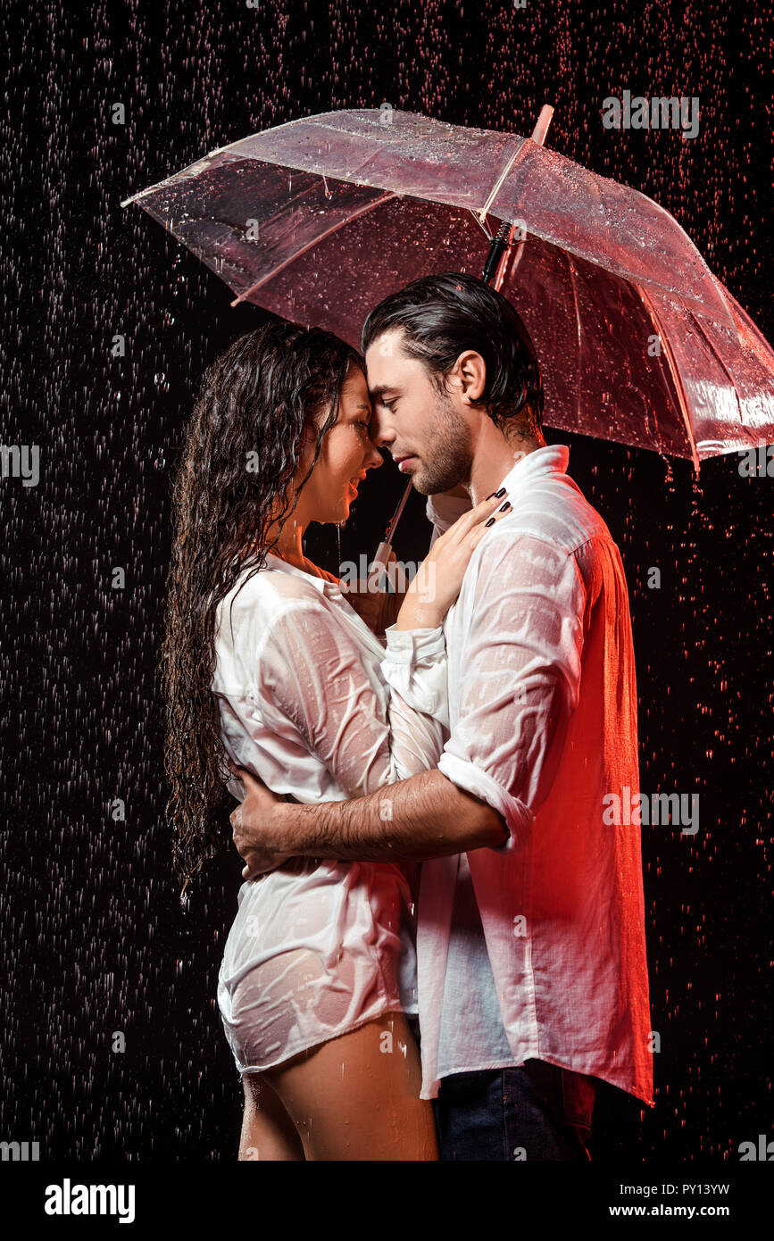 side view of romantic couple in white shirts with umbrella ...