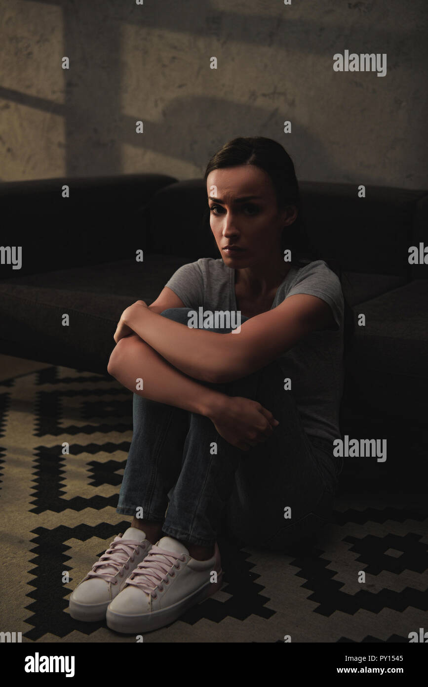 depressed woman hugging her knees while sitting on floor at home Stock ...