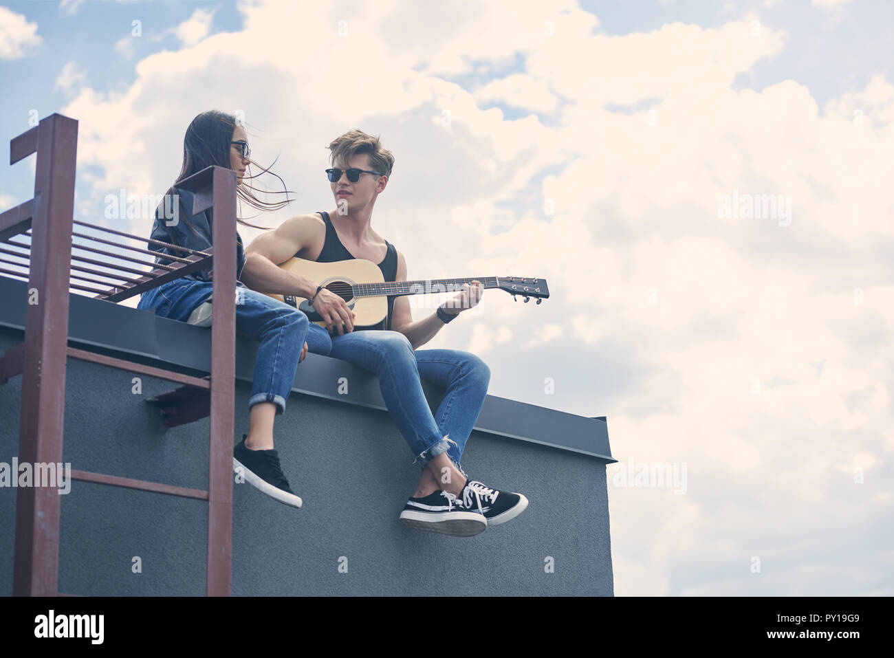 handsome guitarist playing for his attractive asian girlfriend on roof Stock Photo
