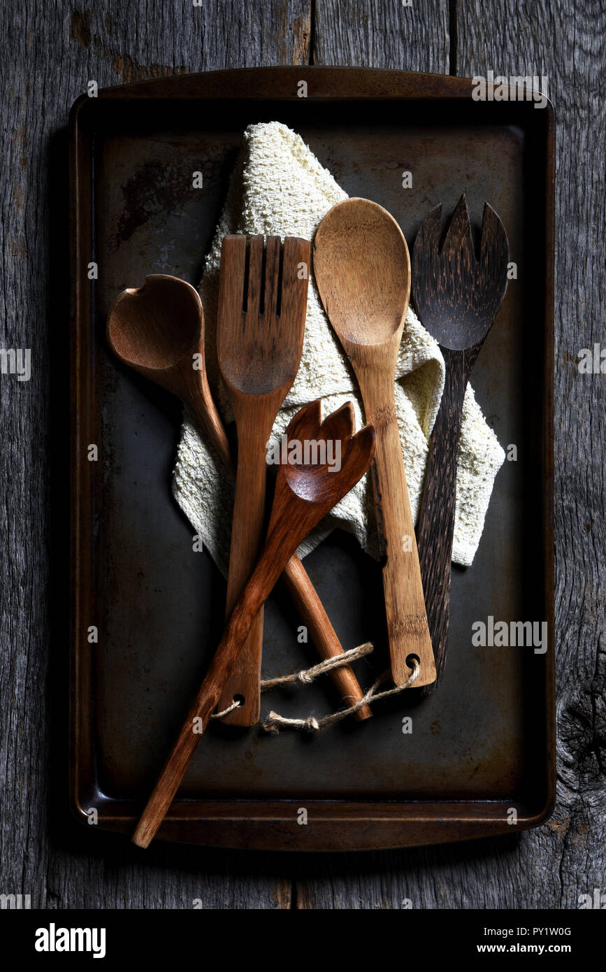 Wooden cooking utensils on a baking sheet, on a rustic wood table with strong side light. Stock Photo