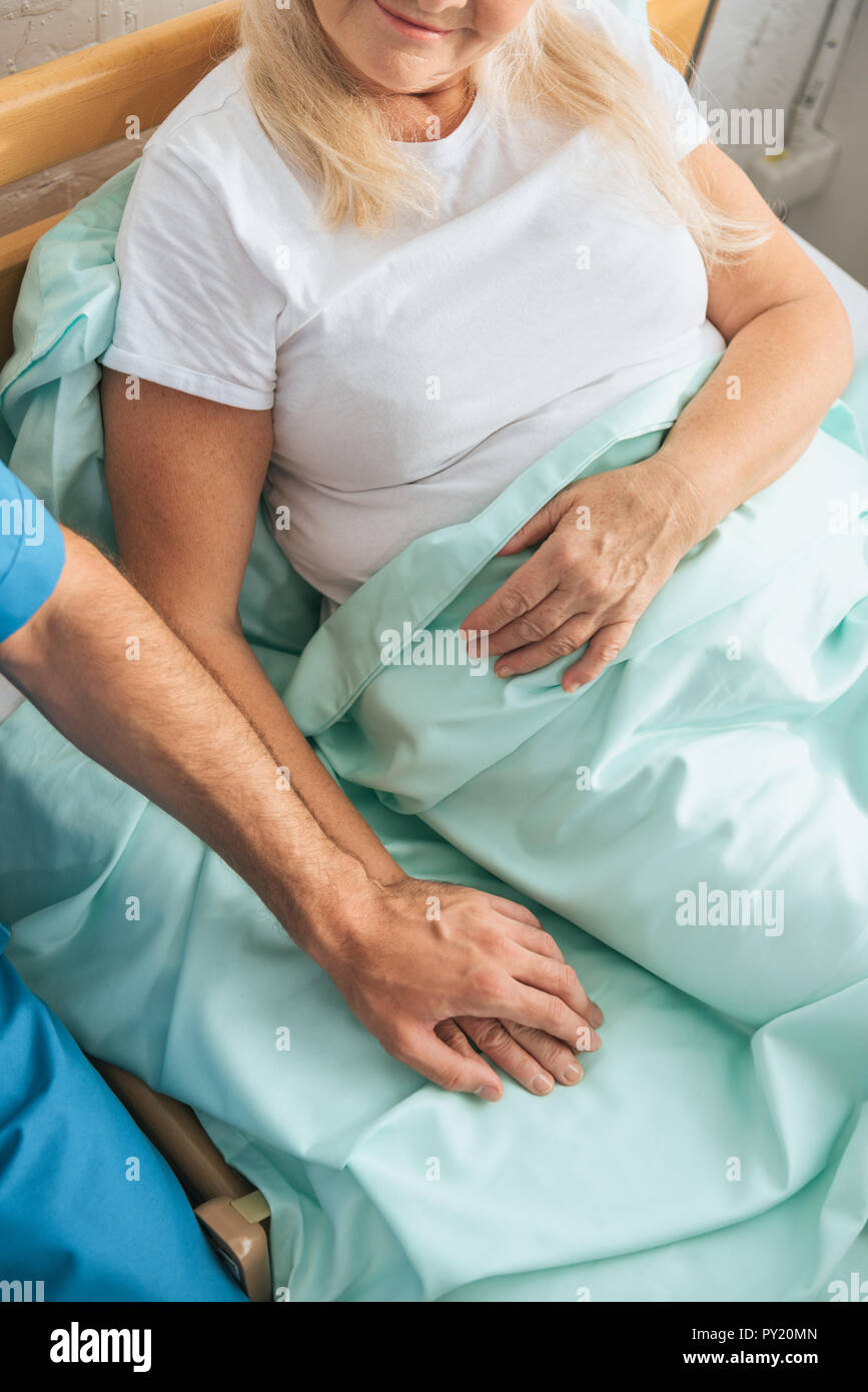 partial view of male nurse holding hand of sick senior woman lying in  hospital bed Stock Photo - Alamy