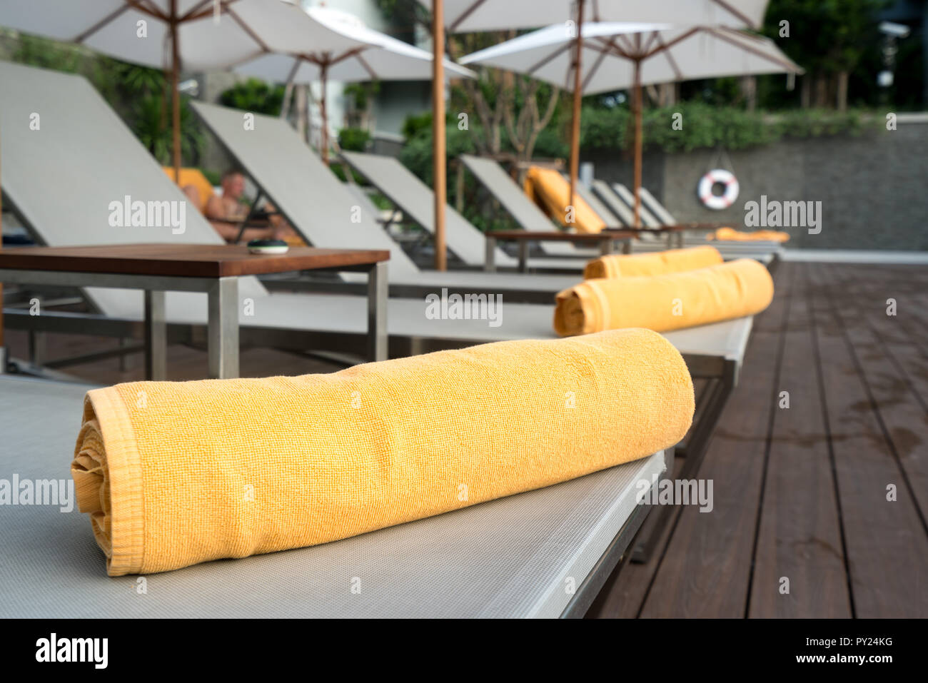 Rolled up orange towel on a sun lounger background of pool in resort or hotel. Stock Photo