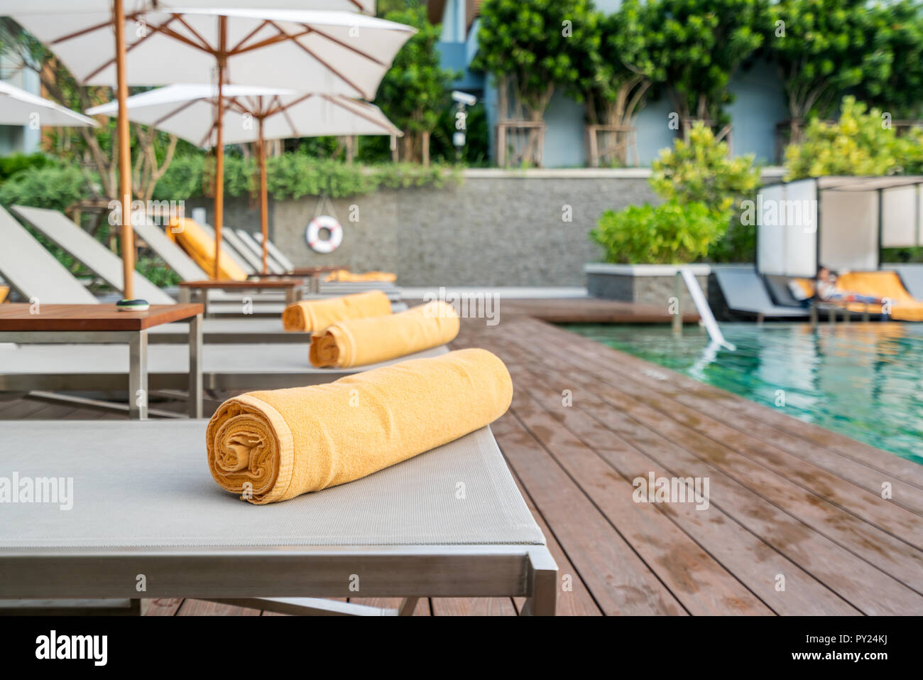 Rolled up orange towel on a sun lounger background of pool in resort or hotel. Stock Photo