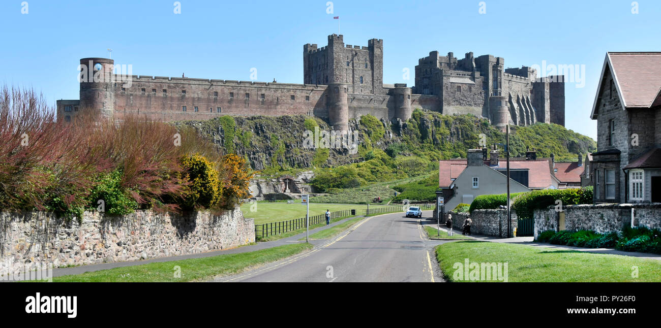 Road out of Bamburgh village panoramic landscape & dramatic backdrop of historical Bamburgh Castle on coast of Northumberland North East England UK Stock Photo