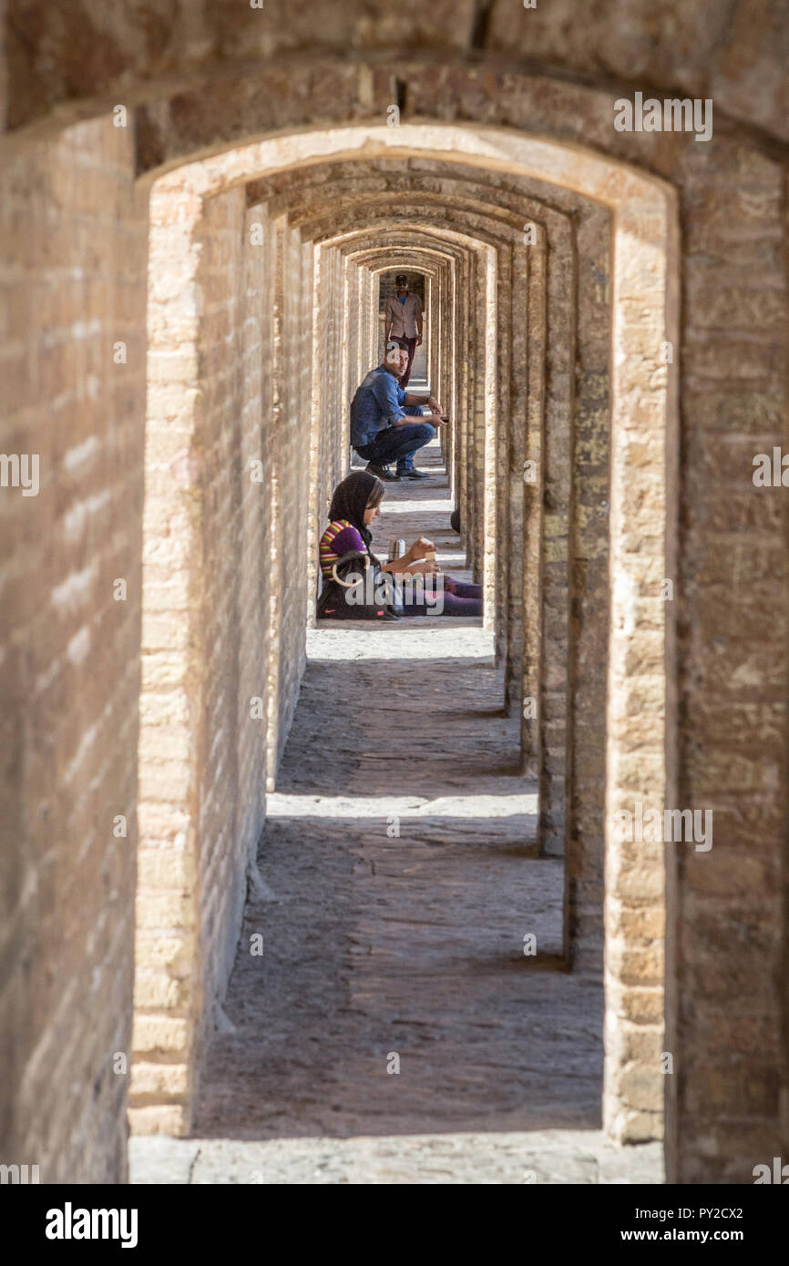 ISFAHAN, IRAN - AUGUST 20, 2016: Perspective of the ancient stone arches of the Si o Seh Pol bridge with Iranian people, men and women, sitting. It is Stock Photo