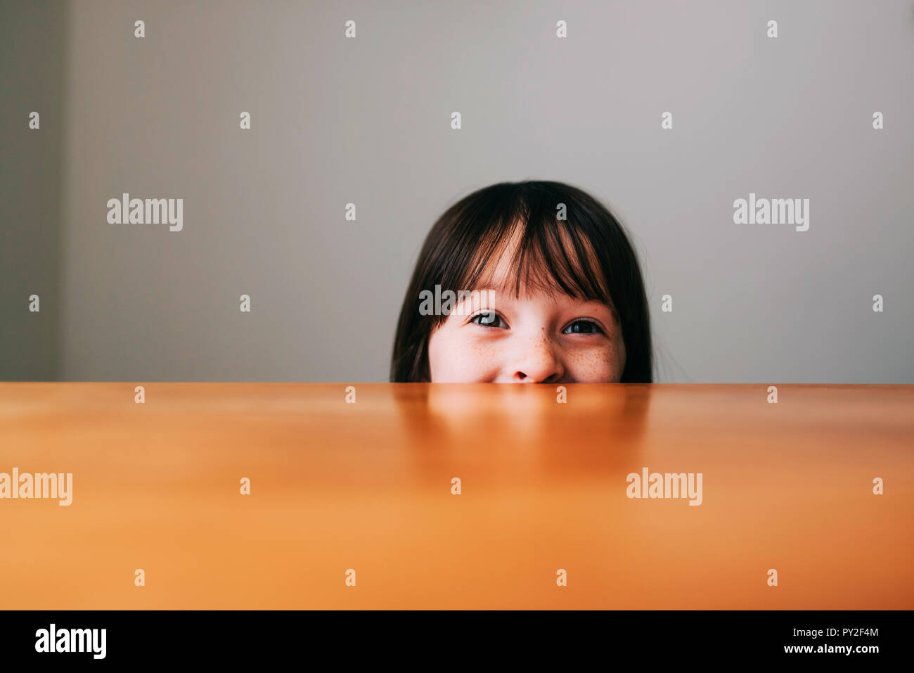 Girl hiding behind a table Stock Photo