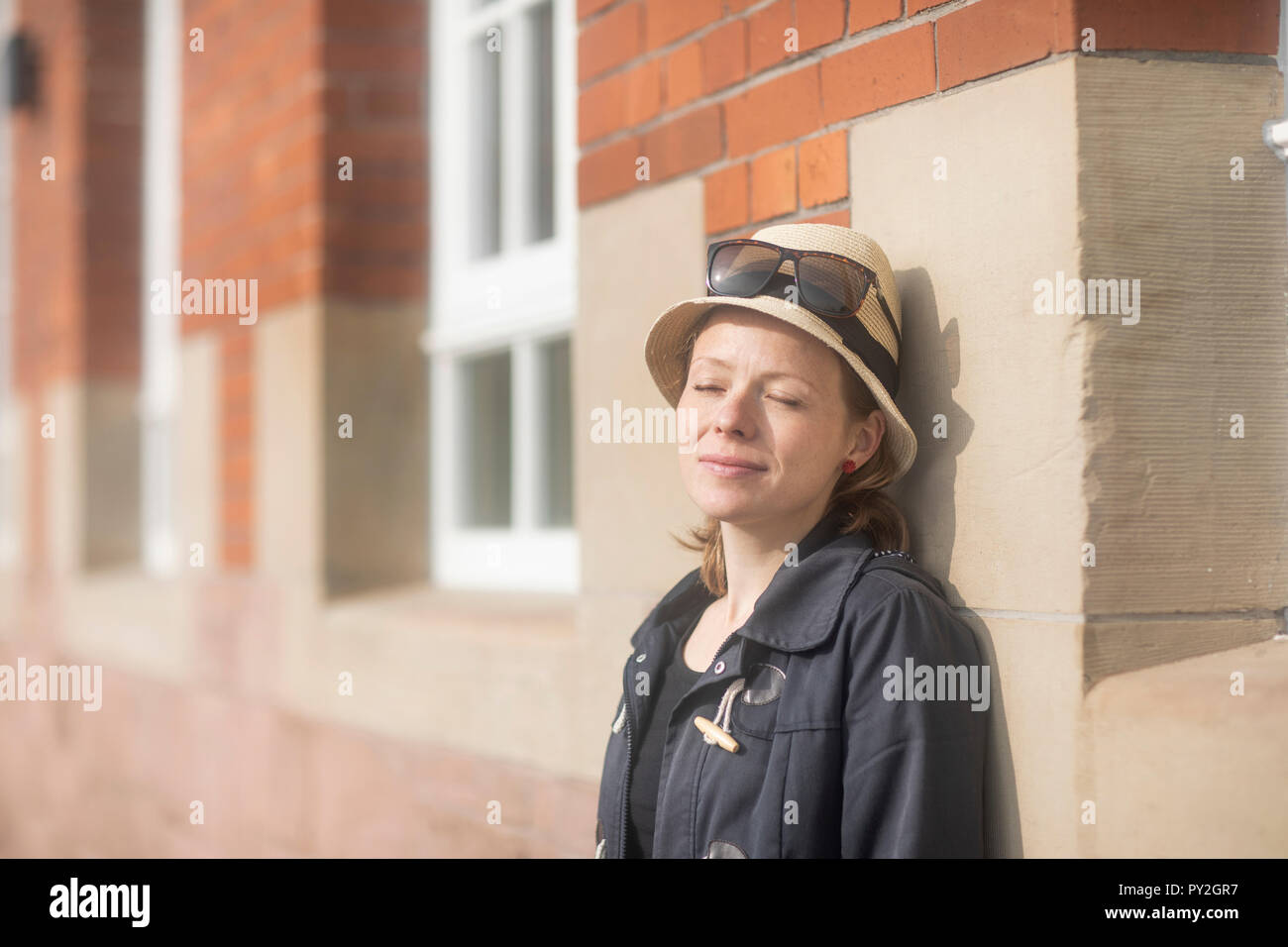 Portrait of a smiling woman standing in street leaning against a wall Stock Photo