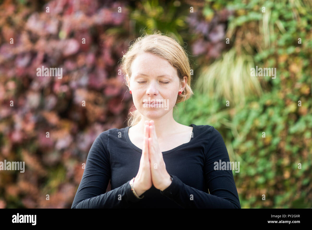 Portrait of a woman standing in the park with her hands in prayer position Stock Photo