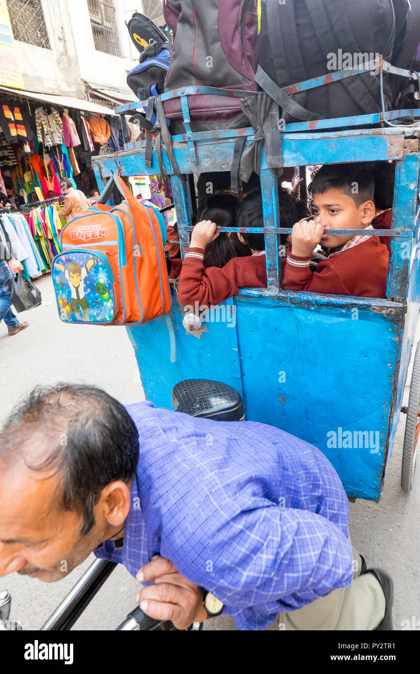 Young middle class Indian children being transported to school in a small wheeled carriage pulled by a man Stock Photo