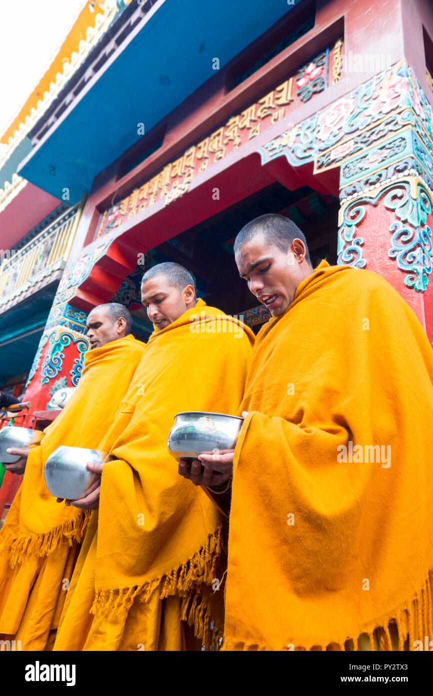 3 Buddhist monks in Saffron robes seeking alms outside temple in Darhamshala , India Stock Photo