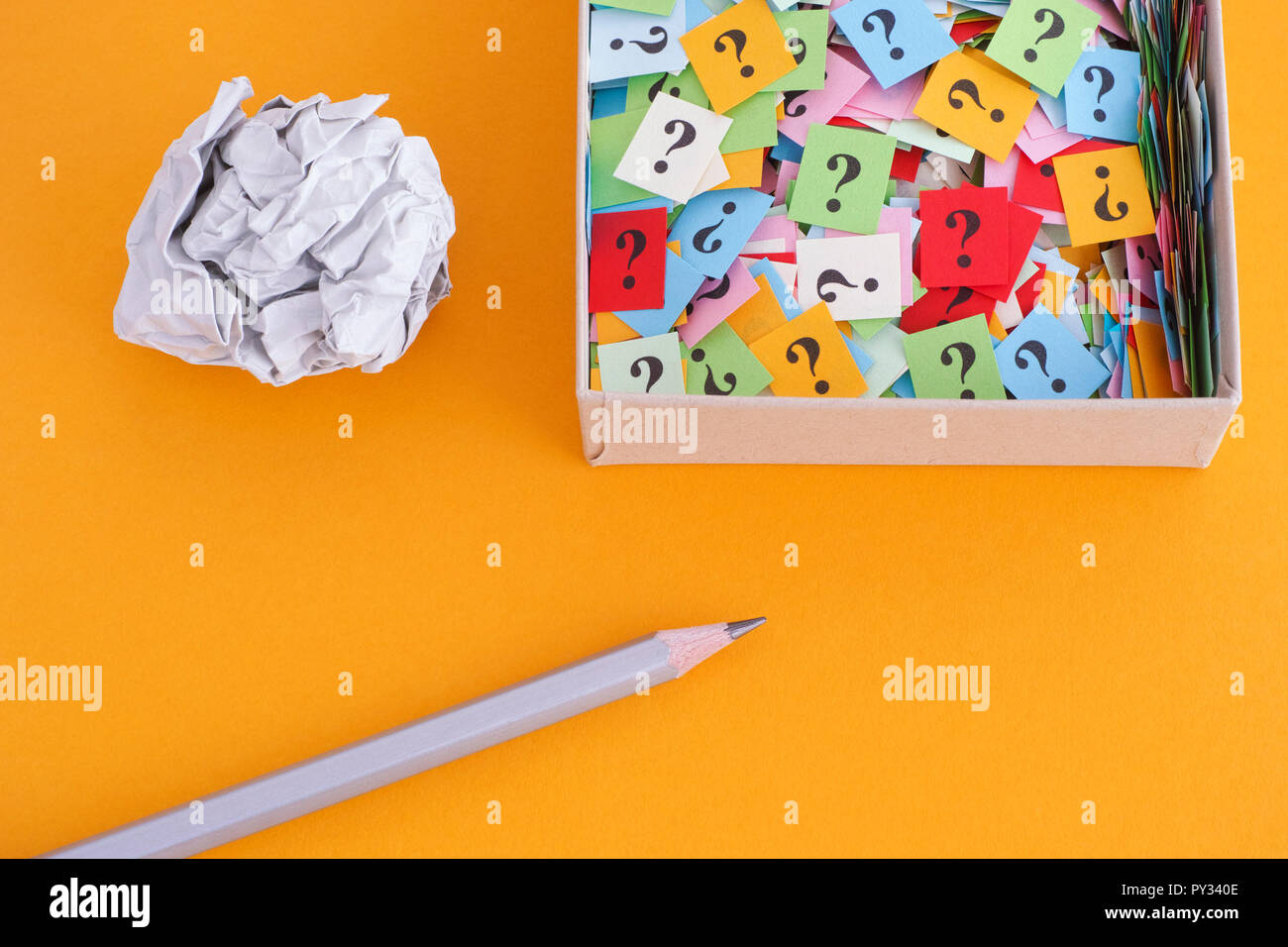Pencil with crumpled paper ball and question marks in a paper box on yellow background. Concept image. Close up. Stock Photo