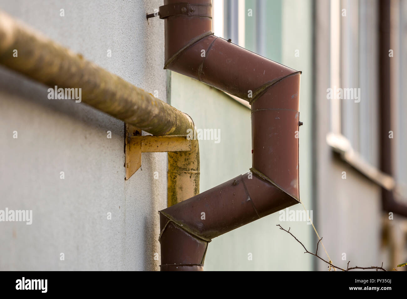 Close up detail of old dirty painted yellow natural gas and brown gutter rain water pipes fastened to white house wall safety danger old and modern