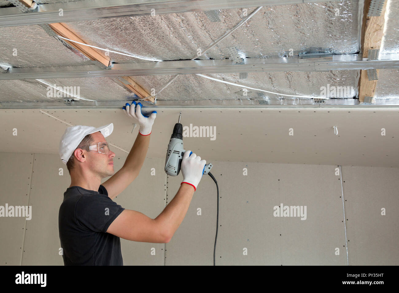 Young Man In Goggles Fixing Drywall Suspended Ceiling To Metal