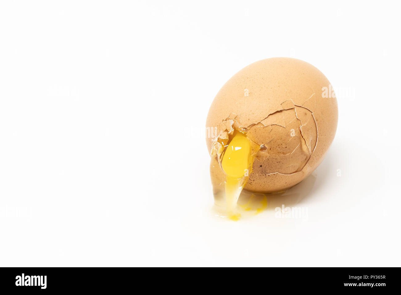Broken brown egg on the white surface. Yolk spilling out through the crack. Stock Photo