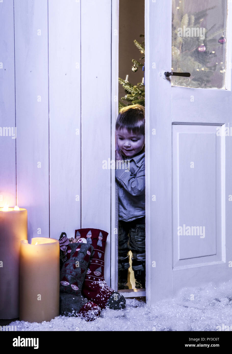 Kleiner Junge schaut durch weihnachtliche Tuere Stock Photo