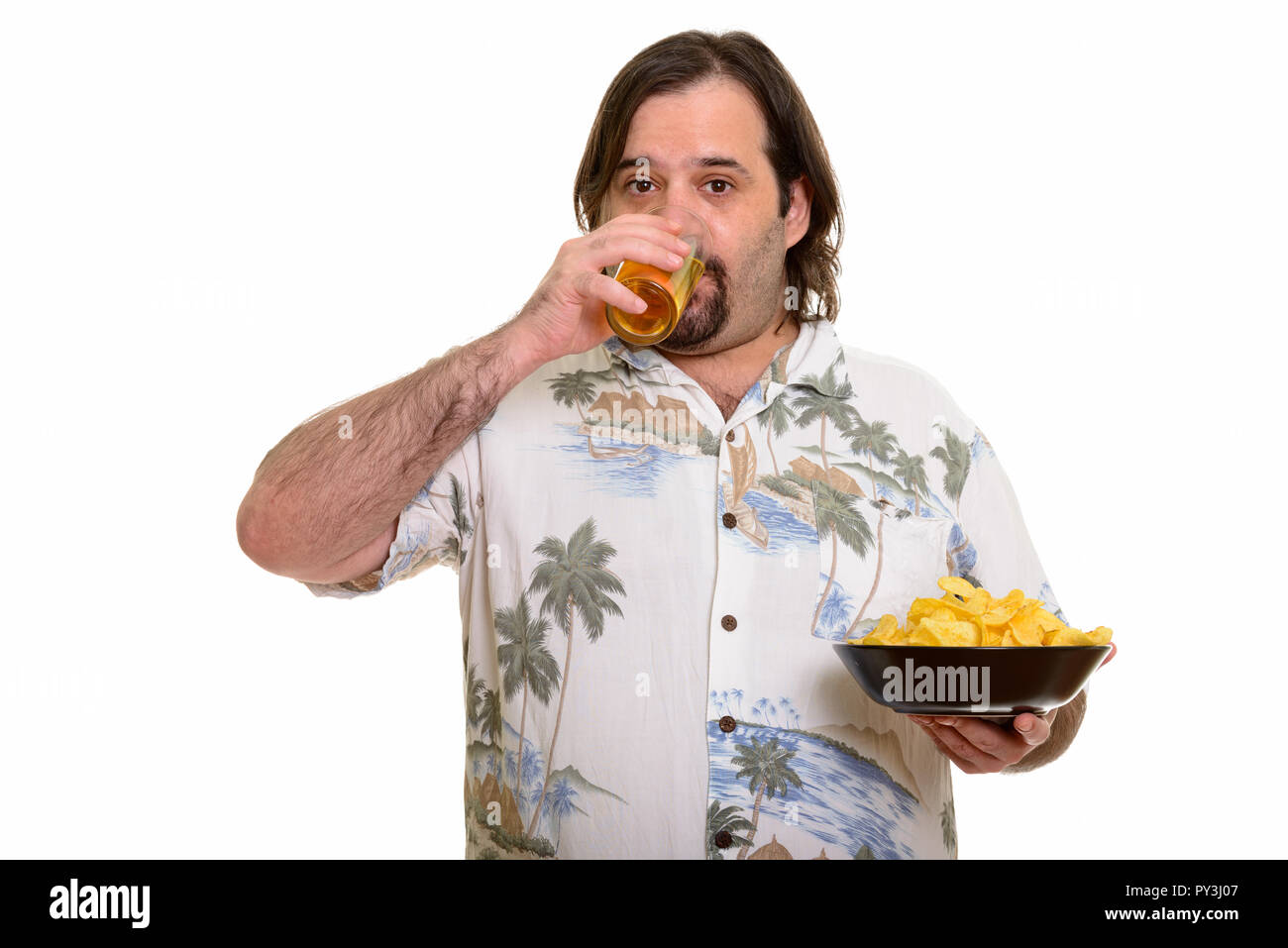 Fat Caucasian man drinking beer and holding bowl of chips ready  Stock Photo