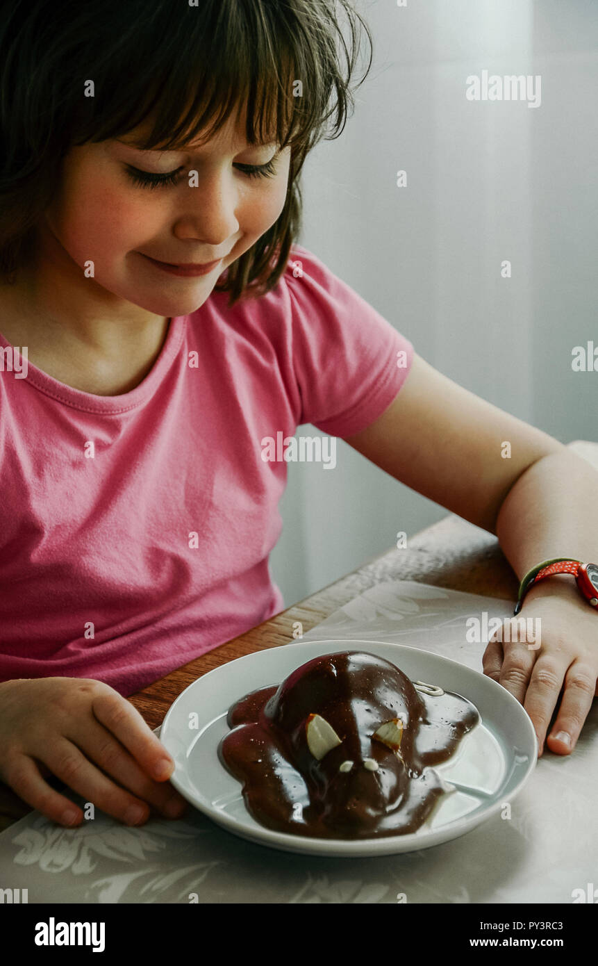 Pear halves coated with chocolate glaze and decorated like a mouse. Creative food, funny dessert for picky eaters. Little girl sitting at the table. Stock Photo