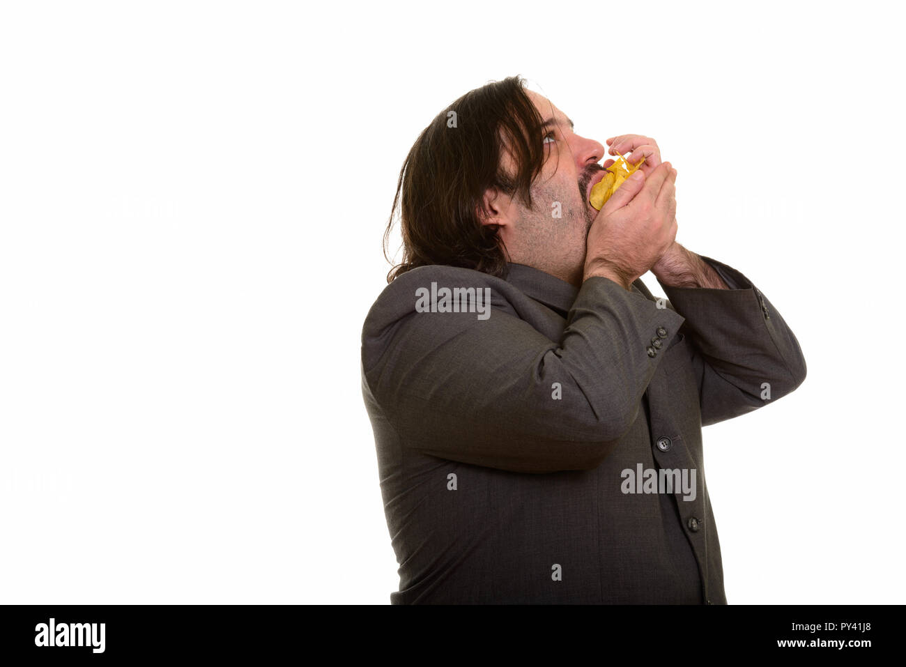 Fat Caucasian businessman eating mouthful of chips Stock Photo