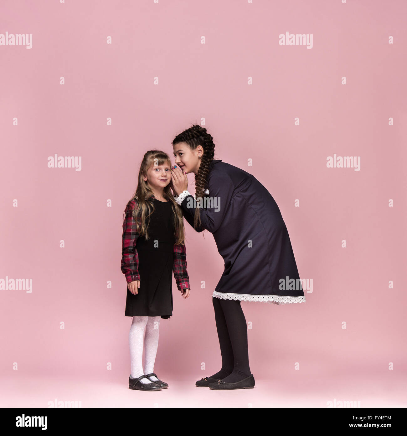 Cute smiling happy stylish children on pink background. Beautiful stylish teen girls standing together and posing at studio. Classic style. Kids fashion and emotions concept. Stock Photo