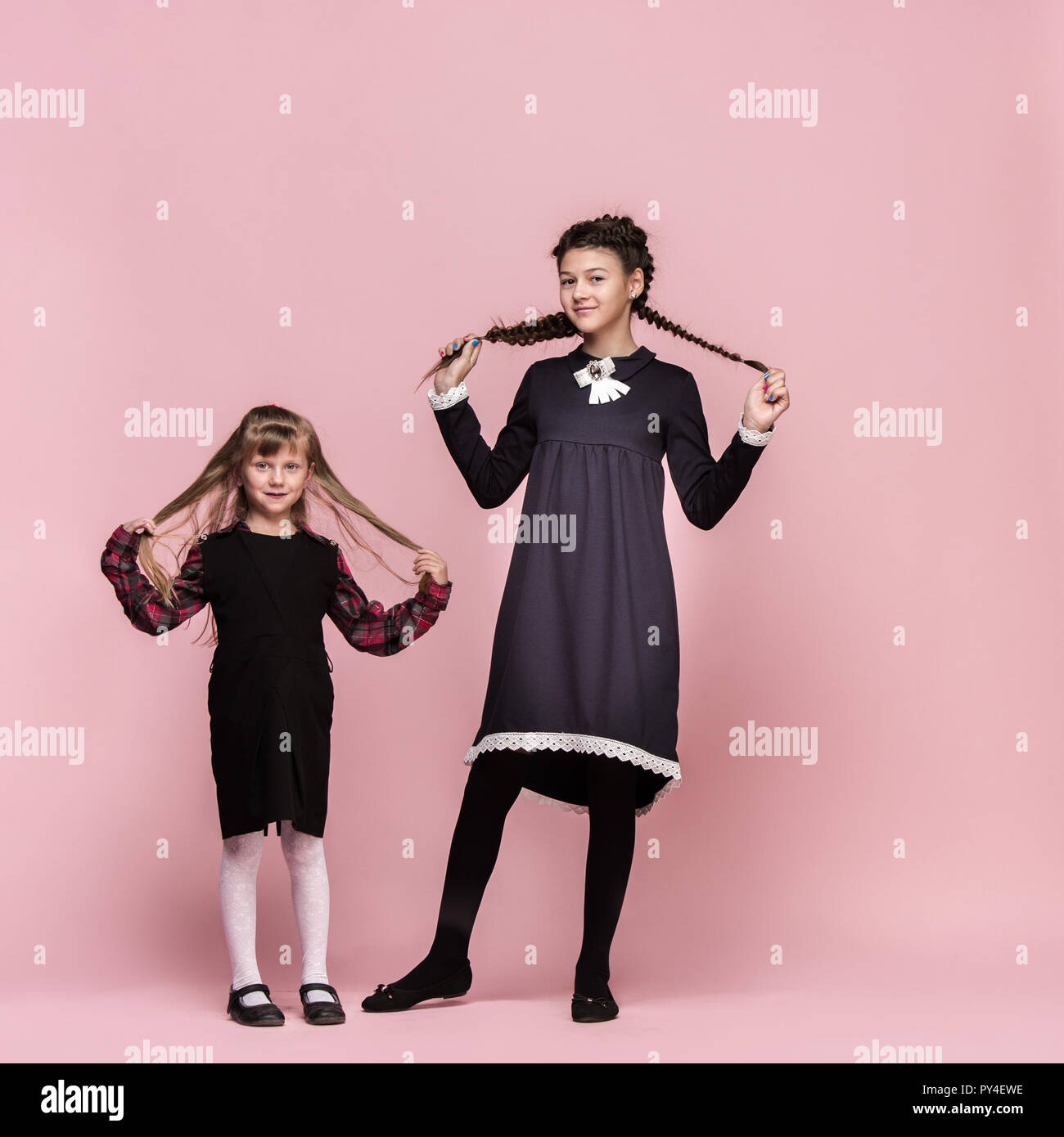 Cute smiling happy stylish children on pink background. Beautiful stylish teen girls standing together and posing at studio. Classic style. Kids fashion and emotions concept. Stock Photo