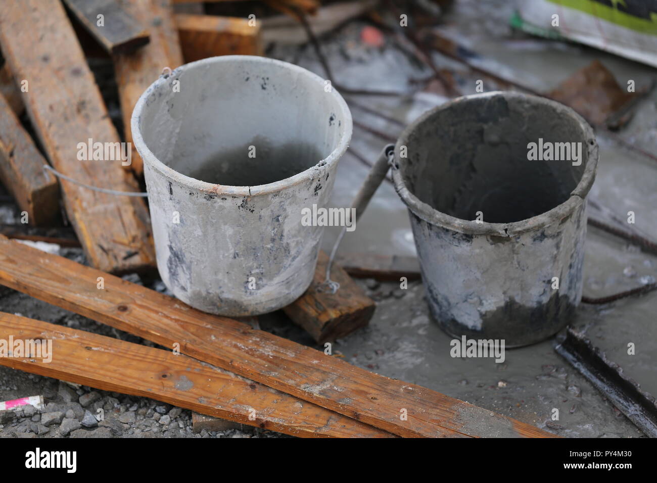 Two Buckets In Construction Site.  Two empty buckets near dirty used planks. White bucket and gray bucket in a messy construction site. Stock Photo