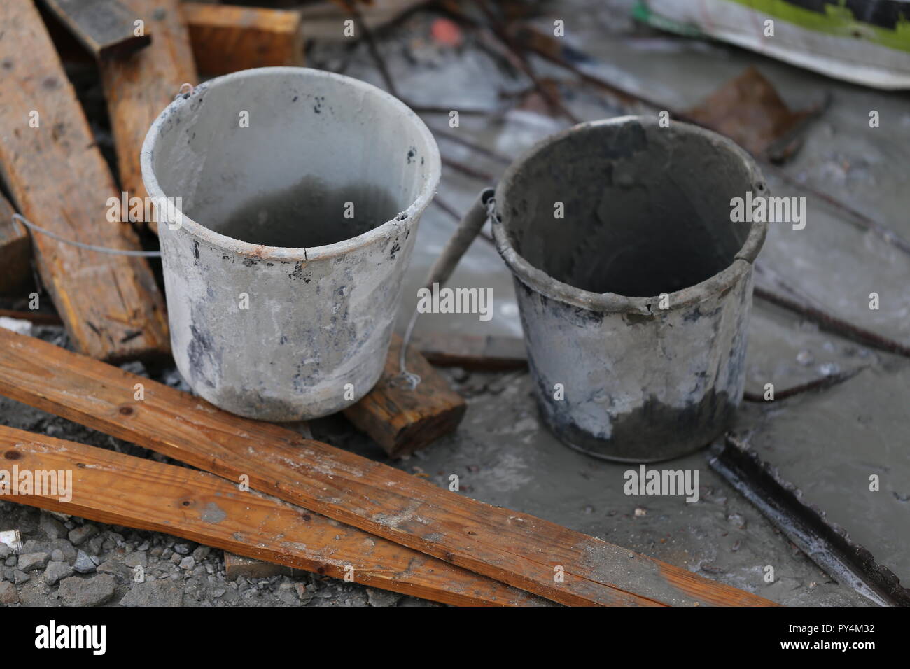 Two Buckets In Construction Site.  Two empty buckets near dirty used planks. White bucket and gray bucket in a messy construction site. Stock Photo