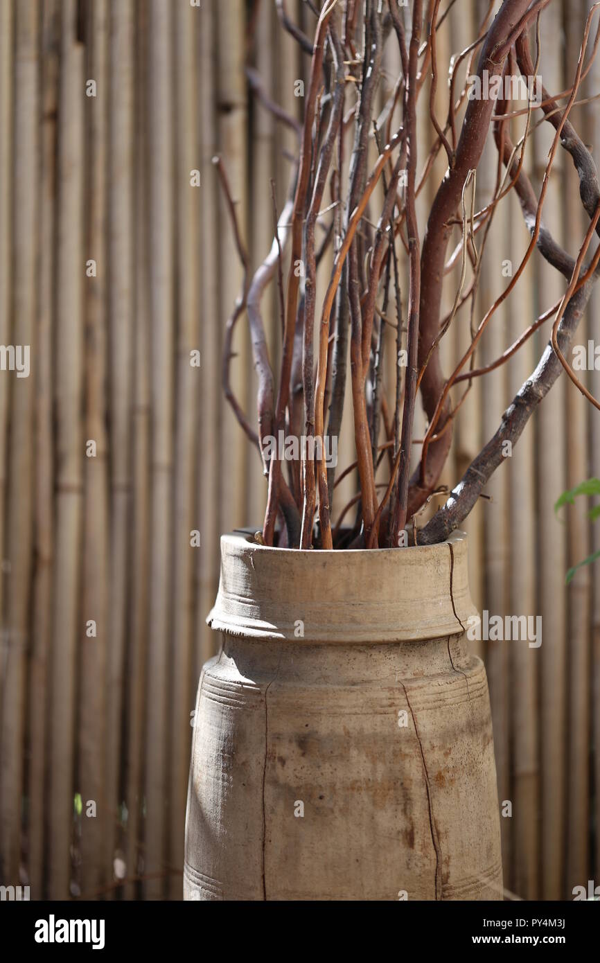 Wooden Vase. Old wooden vase with sticks in the garden in front of babboo fence. Natural decoration producs. Stock Photo