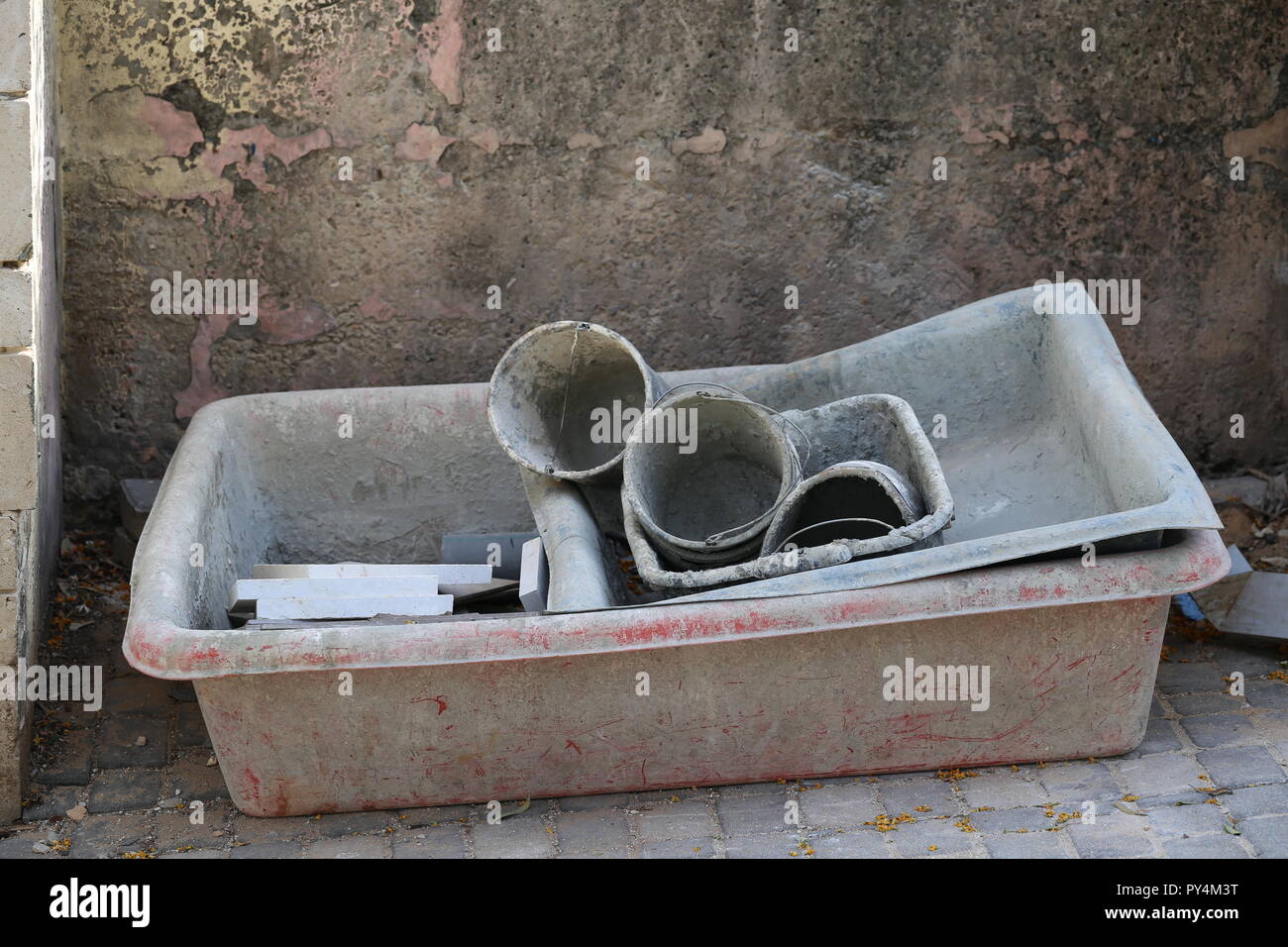 Used Buckets And Containers For Mixing Cement Left Near A Dirty Wall. Three dirty containers for mixing cement and three buckets with concrete residue Stock Photo