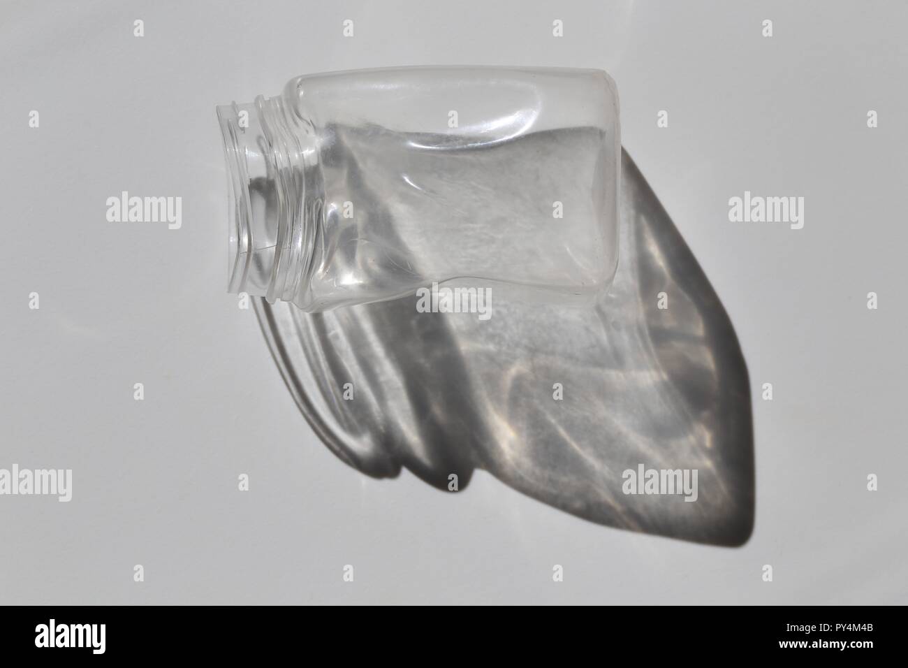 Highlighted Empty Plastic Jar And Its Shadow. Pet Plastic Jar left in the closed car in the high summer heat distorted its shape, white background Stock Photo
