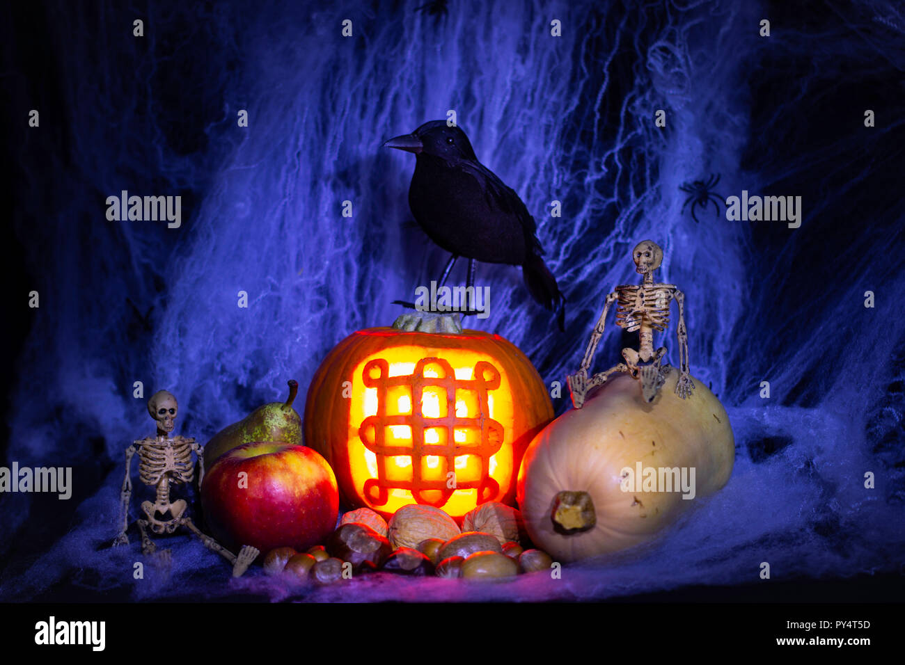 Samhain/Halloween/Celtic New Year still life. Lit carved pumpkin with samhain symbol, fruit, nuts & veg with toy black bird, toy skeletons & fake web. Stock Photo