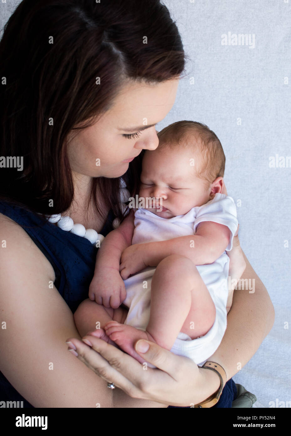 Mother holding sleeping newborn baby close to her chest up looking down