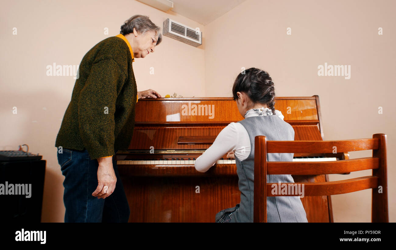 A little girl playing piano on music lesson. A teacher near by her