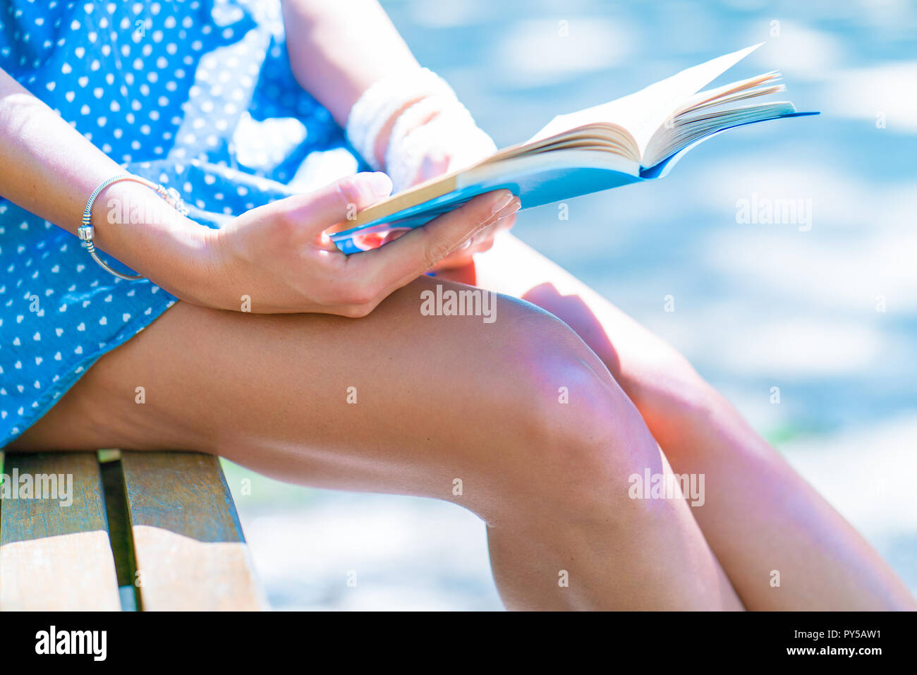 Woman in a blue dress sitting on a bench in a city park and reading a ...