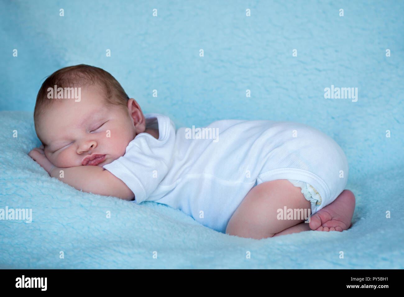 Newborn baby sleeping on his tummy full length side profile blue